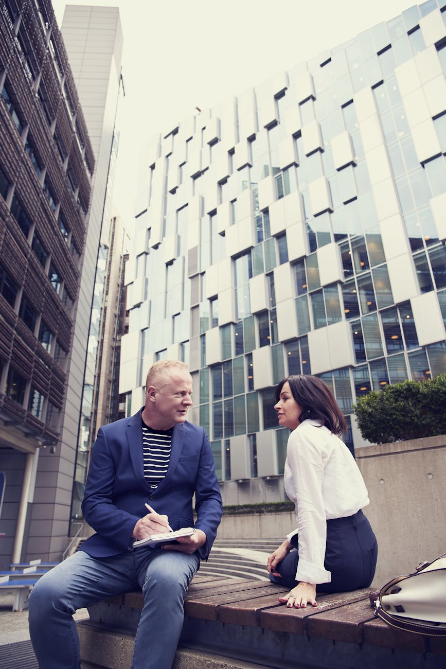 man and woman sitting on wooden bench outside buildings